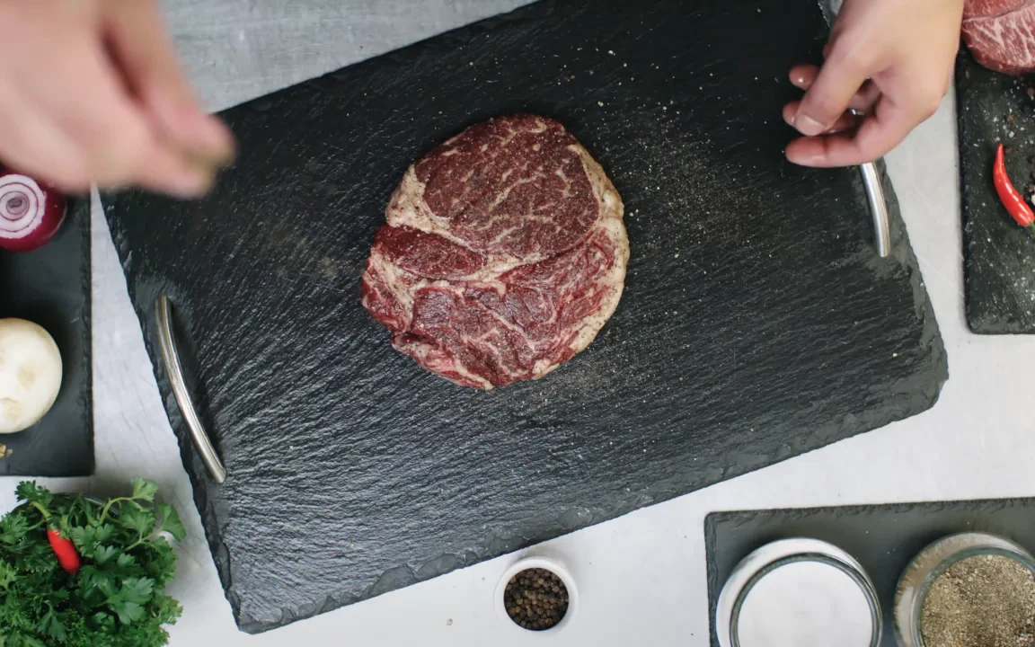 Marbled ribeye being seasoned on a slate board